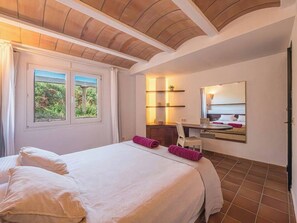 Ein Schlafzimmer mit einem großen Bett, einem Schreibtisch, einem Stuhl, einem Spiegel und einem Fenster mit Vorhängen.