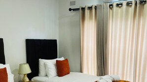 Une chambre d’hôtel avec deux lits, une table de chevet avec une lampe et une fenêtre avec des rideaux.
