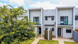 Un immeuble résidentiel moderne à plusieurs étages, doté d’un design épuré et minimaliste, de grandes fenêtres et d’un jardin bien entretenu.