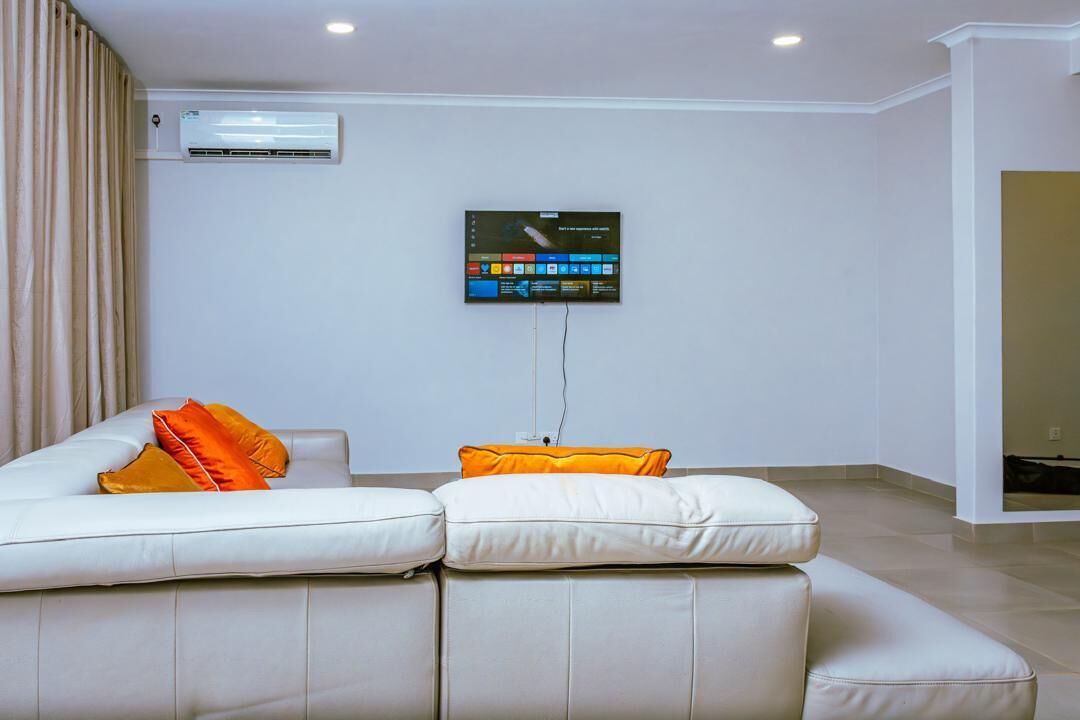 Un salon moderne avec un canapé en cuir blanc, un téléviseur à écran plat fixé au mur et un appareil de climatisation installé sur le mur.