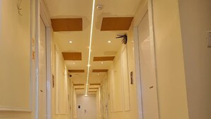 Corredor longo e estreito de hotel, com portas em ambos os lados, iluminação embutida e chão brilhante.