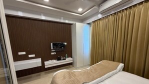 Quarto de hotel com cama, televisão, minibar e cortina.
