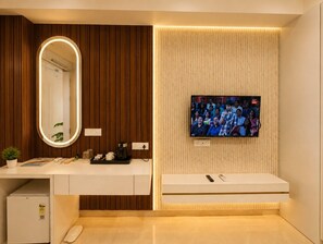 A modern bathroom with a vanity, a mirror, a television mounted on the wall, and a small refrigerator. - The Aura Hotel (Faizabad)
