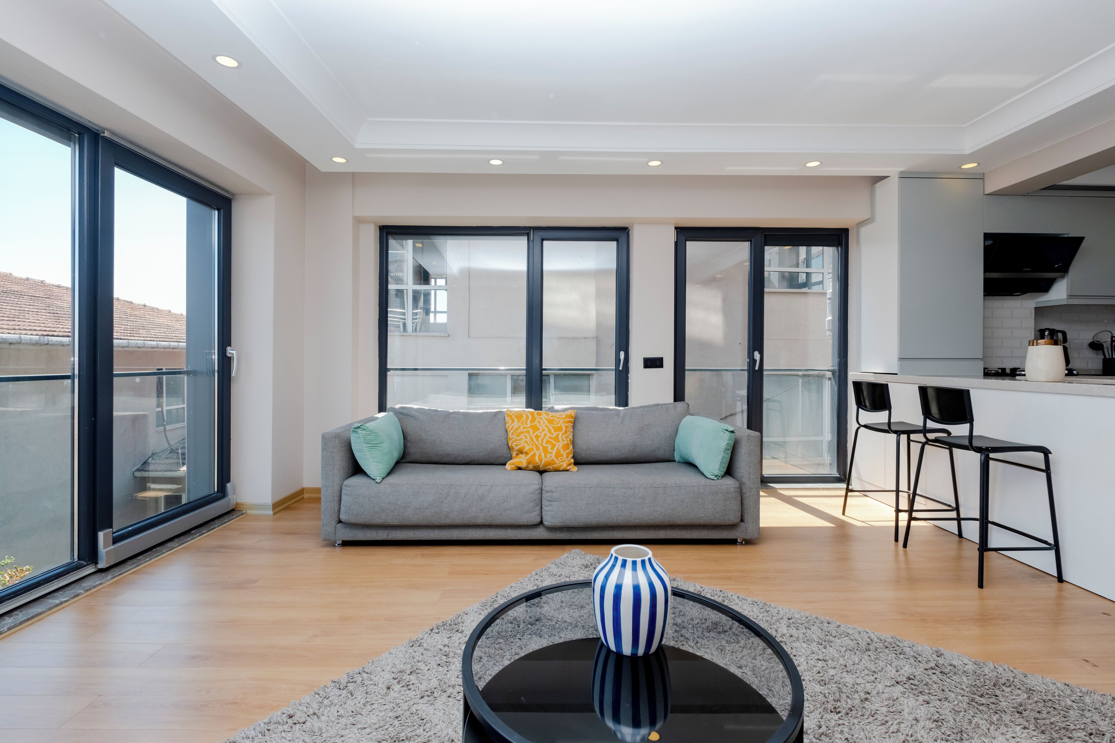 A modern living room with a grey sofa, a coffee table, and a kitchen area with bar stools.