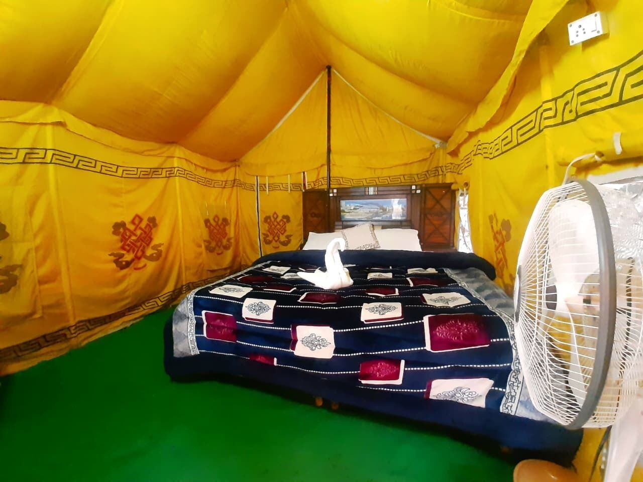 A tent with a bed, a fan, and a green floor.