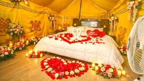 A tented room with a bed adorned with rose petals and a heart-shaped decoration, surrounded by floral arrangements and candles. - Ronak Happy Stay River Side Camping (Balichauki)