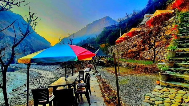 A terrace with outdoor seating, a stone pathway, and a view of mountains. - Ronak Happy Stay River Side Camping (Balichauki)