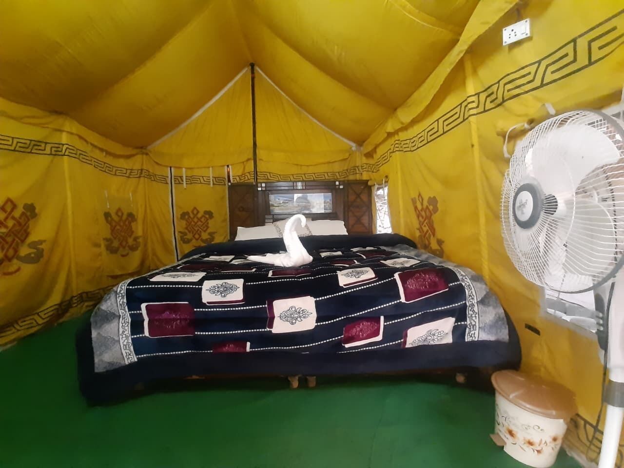Une pièce aménagée comme une tente, avec un lit, un ventilateur et un seau.