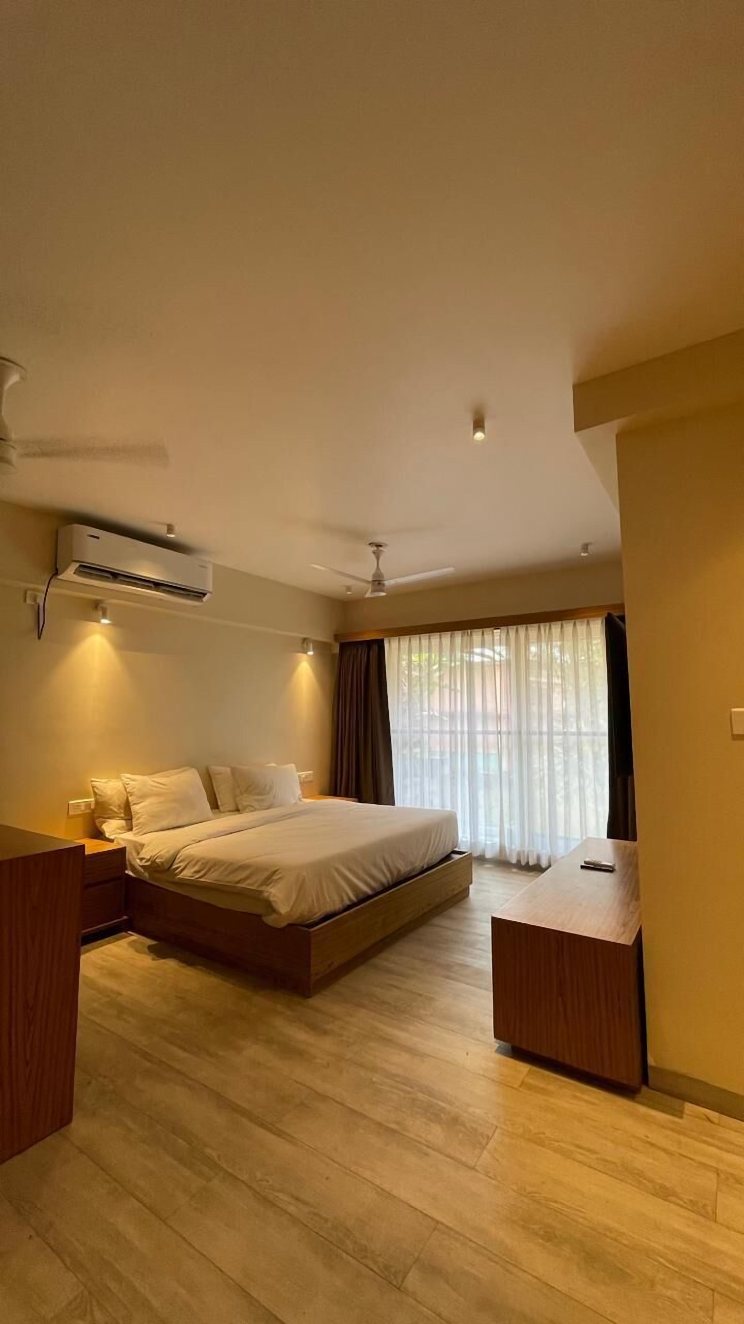 Un dormitorio moderno con una cama grande, un ventilador de techo, un equipo de aire acondicionado y vistas al exterior a través de cortinas traslúcidas.