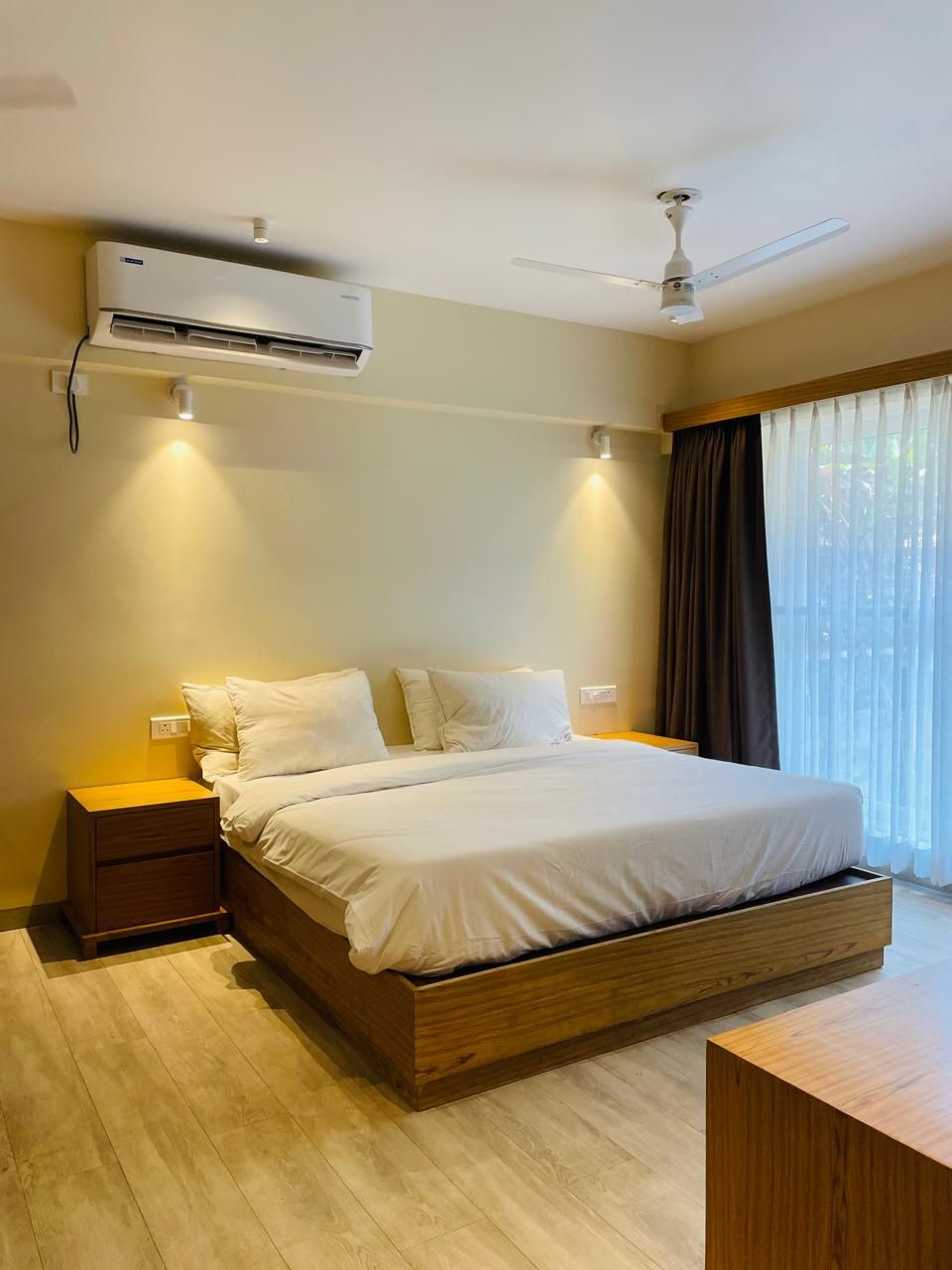 Un dormitorio moderno con una cama grande, mesitas de noche, aire acondicionado, ventilador de techo y una ventana con cortinas.