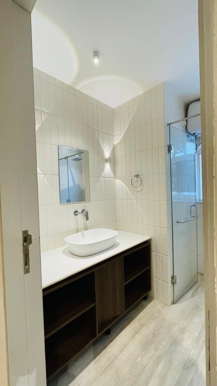 A modern bathroom with a white sink, dark wooden vanity, and a glass shower enclosure.