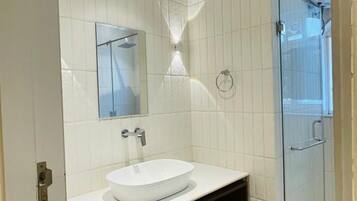 A modern bathroom with a white sink, dark wooden vanity, and a glass shower enclosure.