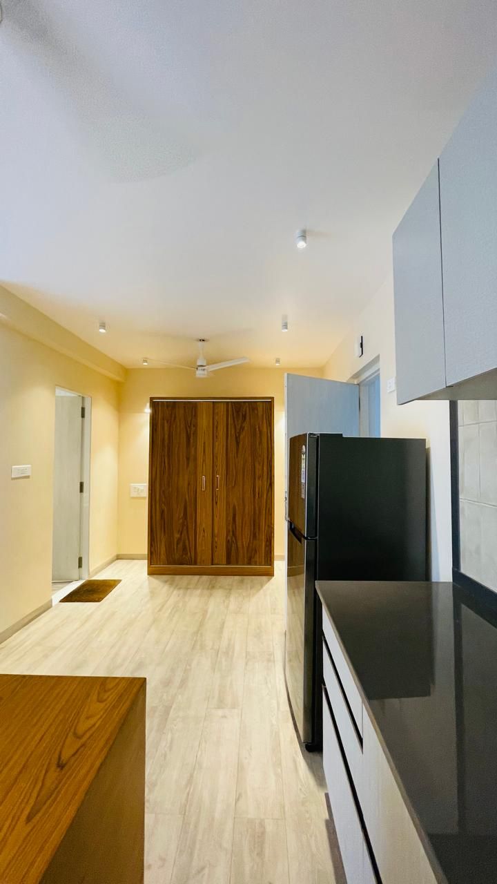 A modern kitchen with a wooden wardrobe, a black refrigerator, and a light-colored floor.