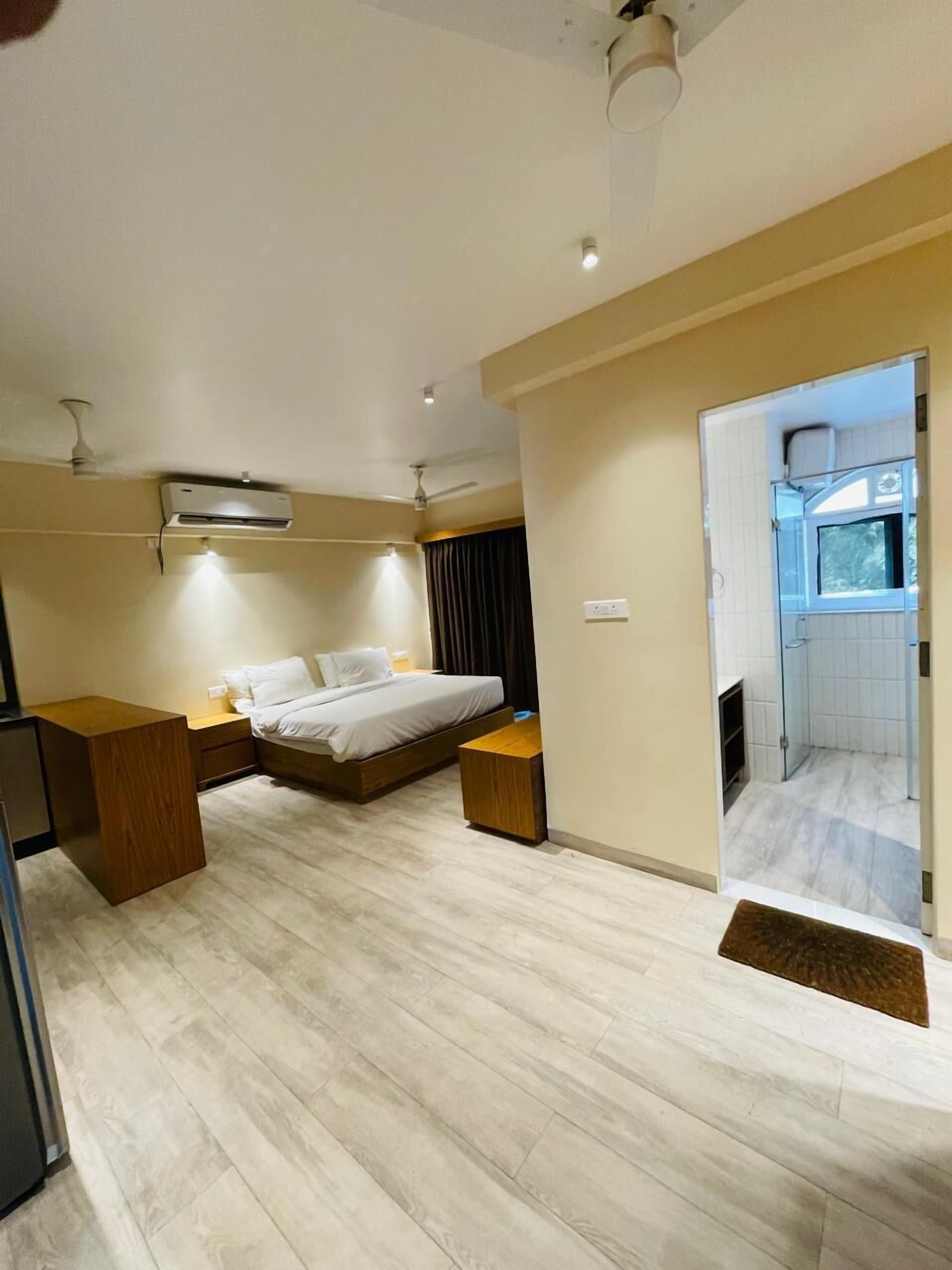A modern hotel room with a bed, bedside tables, an air conditioning unit, and a view of the bathroom.