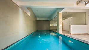 Una piscina con acqua cristallina, pareti piastrellate e una porta in vetro che dà su una zona coperta.