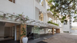 Un edificio moderno con una zona salotto esterna coperta, un vaso bianco di grandi dimensioni e un vialetto in mattoni.