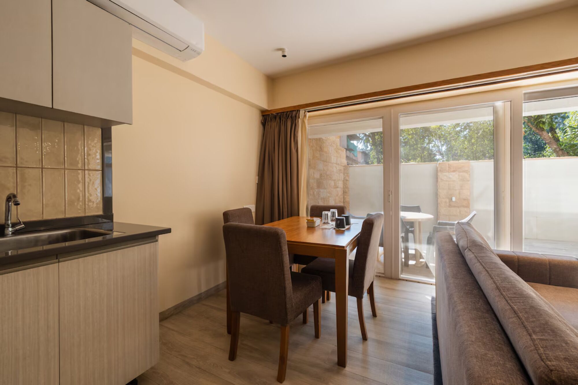 A modern kitchen with a built-in oven, a dining area with a wooden table and chairs, and a sliding glass door leading to an outdoor patio.