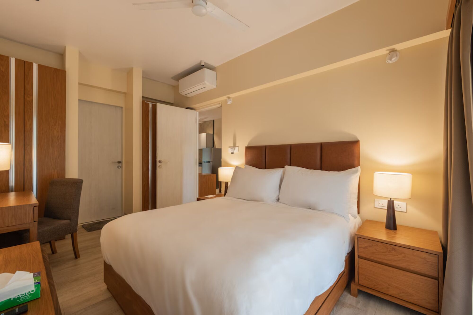 A hotel room with a large bed, bedside tables with lamps, a desk with a chair, and a wardrobe.