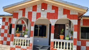 A building with a red and grey brick facade, three arched windows, and a balcony with potted plants. - Gorgeous 3-bedroom house in Kokrobite near the beach (GJ49+MR5 Kokrobite)