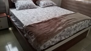 A neatly made bed with floral bedding and a brown throw blanket, a nightstand with a lamp, and a window with blinds. - Gorgeous 3-bedroom house in Kokrobite near the beach (GJ49+MR5 Kokrobite)