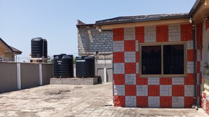 A rooftop with a small structure featuring a checkered pattern, water tanks, and a paved area. - Gorgeous 3-bedroom house in Kokrobite near the beach (GJ49+MR5 Kokrobite)