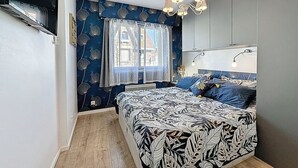 A bedroom with a bed, a window with curtains, a chandelier, and a wall-mounted lamp. - Résidence de la Mer by Interhome (La Bernerie-en Retz)