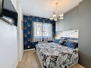 A bedroom with a bed, a window with curtains, a chandelier, and a wall-mounted lamp. - Résidence de la Mer by Interhome (La Bernerie-en Retz)