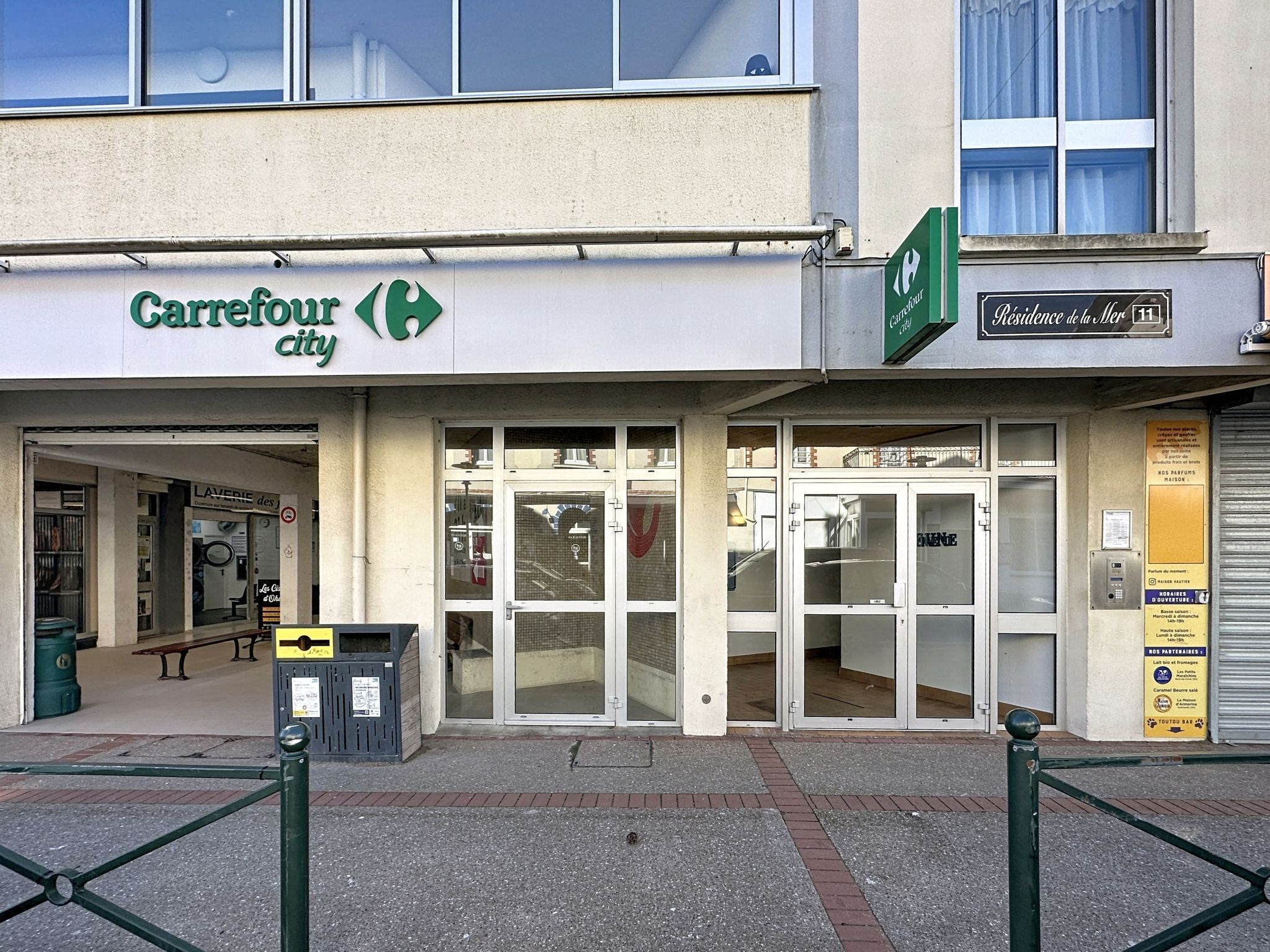 En butikslokal med en Carrefour-skylt, en väl synlig entré och en närliggande byggnad med en skylt som visar texten "Residencia de la Marina".