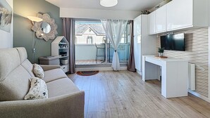 A modern living room with a sofa, a dining area, and a kitchen with a TV. - Résidence de la Mer by Interhome (La Bernerie-en Retz)