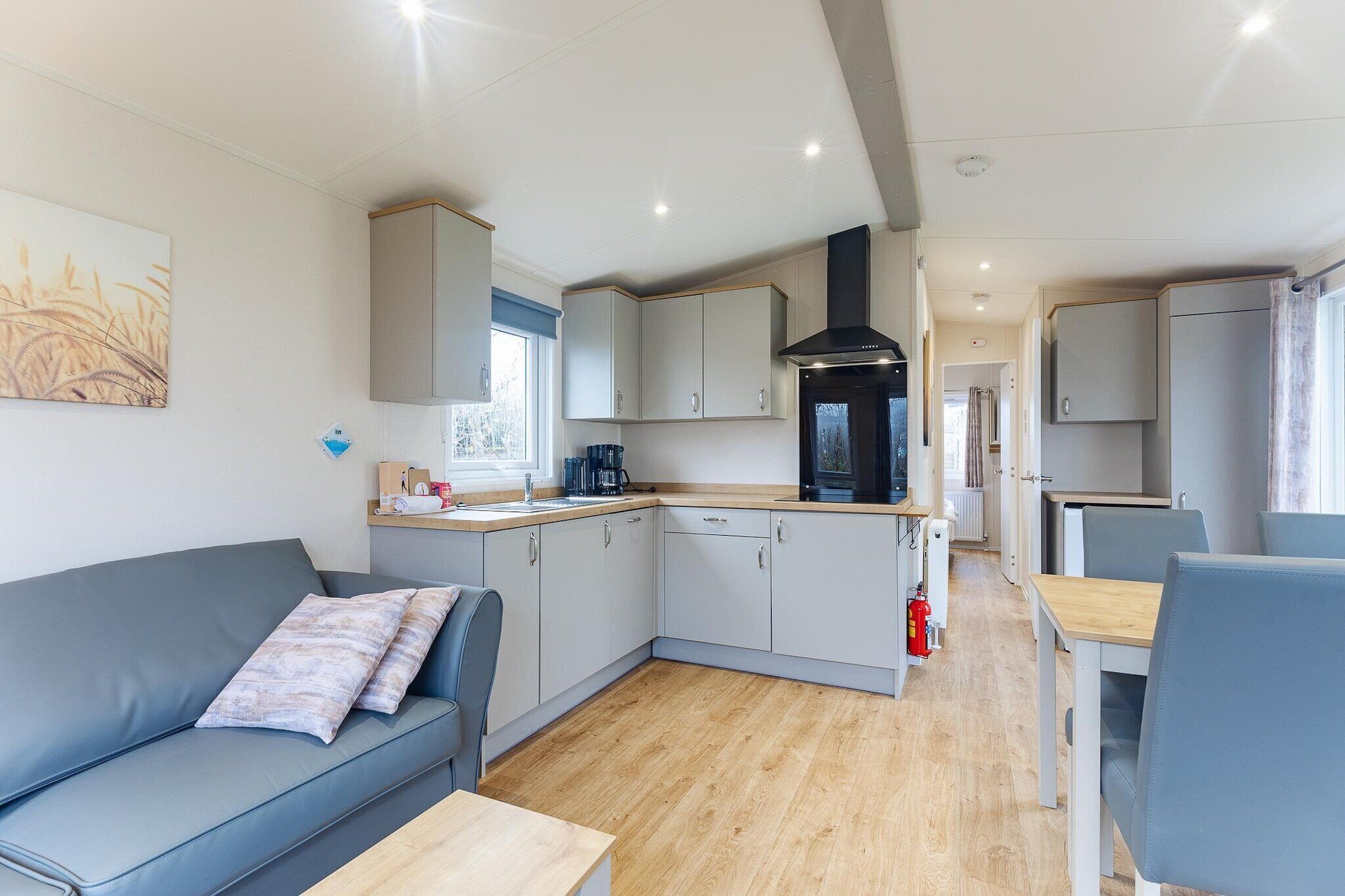 A compact kitchenette with a stove, sink, and cabinets, a sofa with a cushion, and a dining table with chairs.
