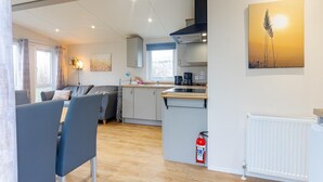 A modern kitchen with a built-in stove, a dining area with a table and chairs, and a living room with a sofa and a painting on the wall.