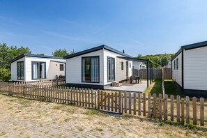 A row of mobile homes with a wooden fence, a patio, and a grassy area. - Bright Beachside Base in Burgh-Haamstede (Burgh-Haamstede)