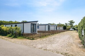 A row of mobile homes with a wooden fence, a dirt path, and a car parked in the background. - Bright Beachside Base in Burgh-Haamstede (Burgh-Haamstede)