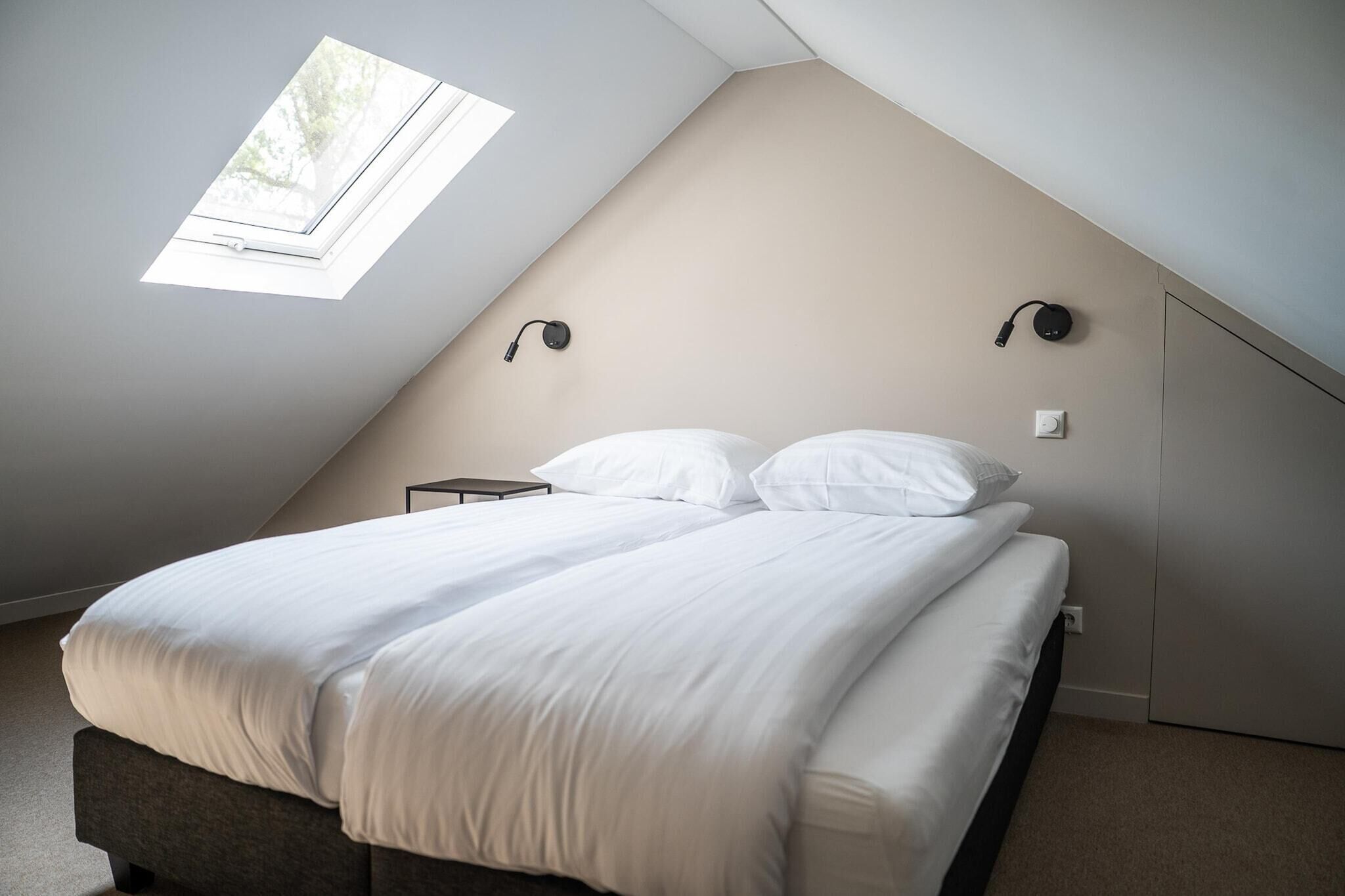 Un dormitorio con cama, un tragaluz y dos lámparas fijadas a la pared.