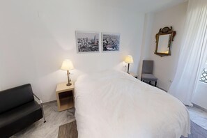 Ein Hotelzimmer mit einem Bett, zwei Nachttischlampen, einem Sessel, einem kleinen Tisch und zwei gerahmten Bildern an der Wand.
