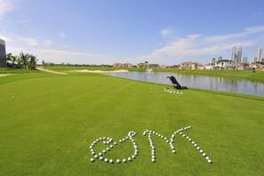 A golf course with a water hazard, a golf bag, and golf balls arranged in a pattern. - Cozy Elviria Beachside Apartment (Marbella)
