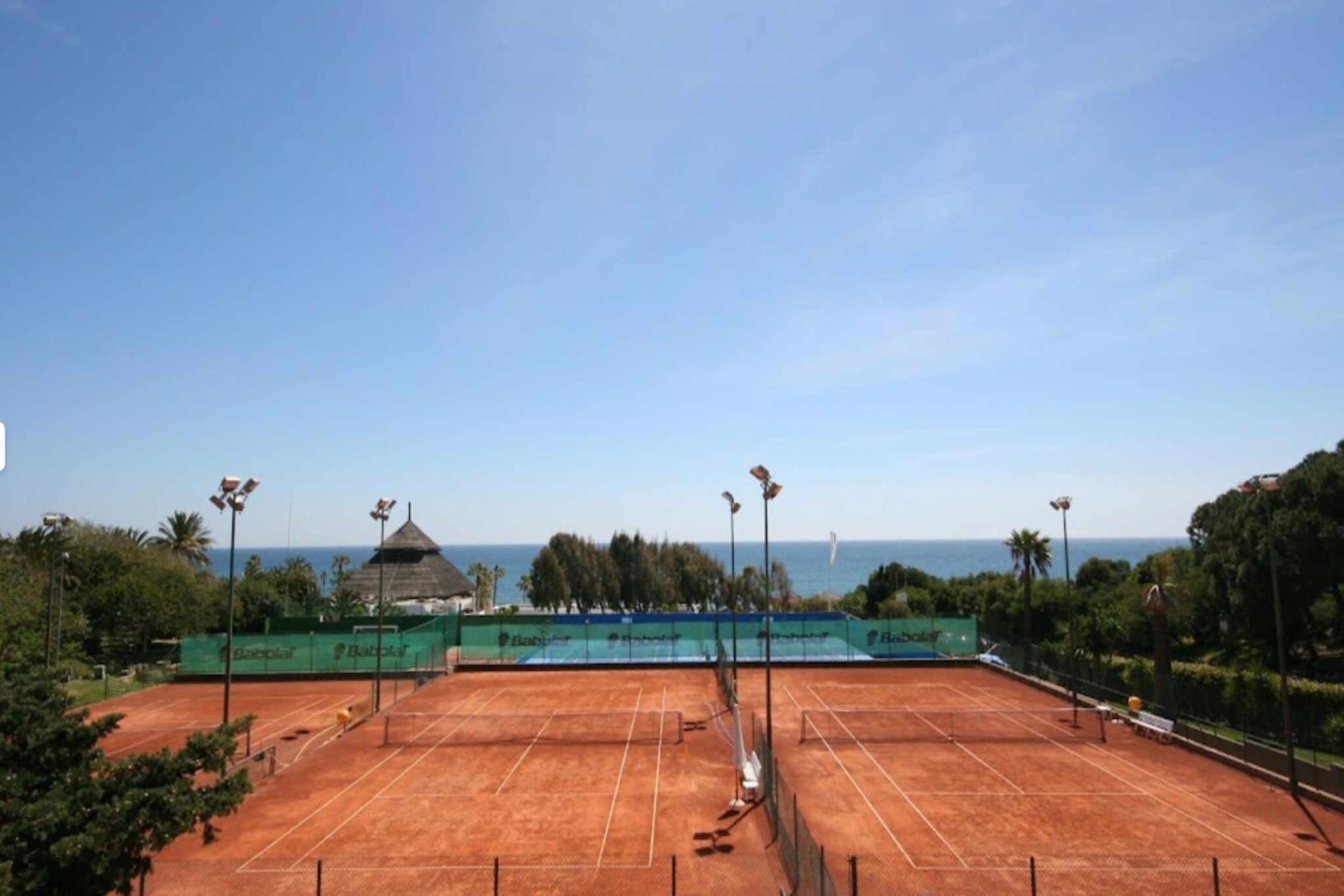 A tennis court with a clear view of the ocean and a dome structure in the background.