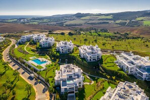 A modern residential complex with multiple white buildings, a winding road, and a large swimming pool. - Mountain View Resort in Solenzara (Casares)