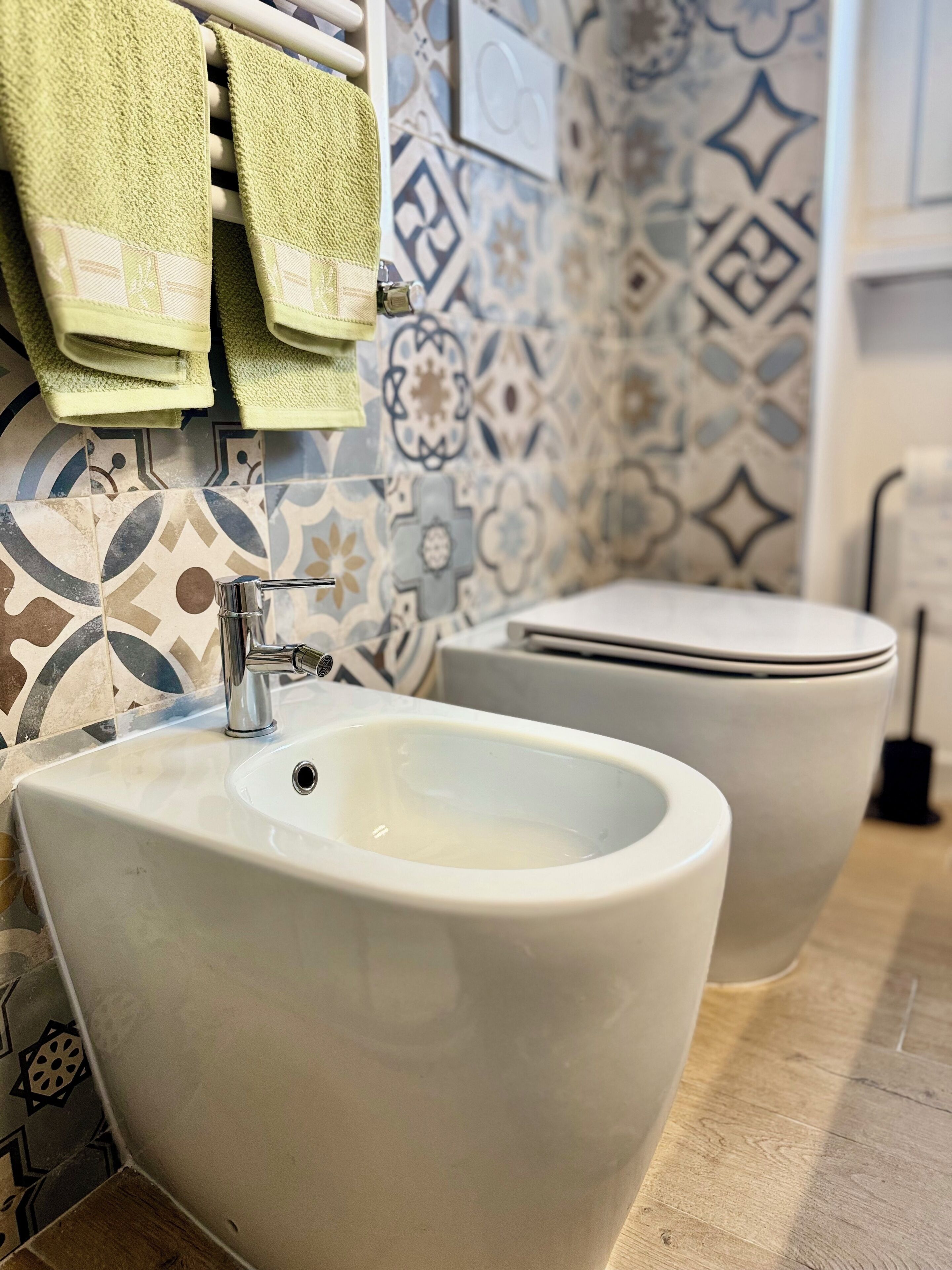 A bathroom with a bidet, a sink, and a toilet. The walls are decorated with patterned tiles.