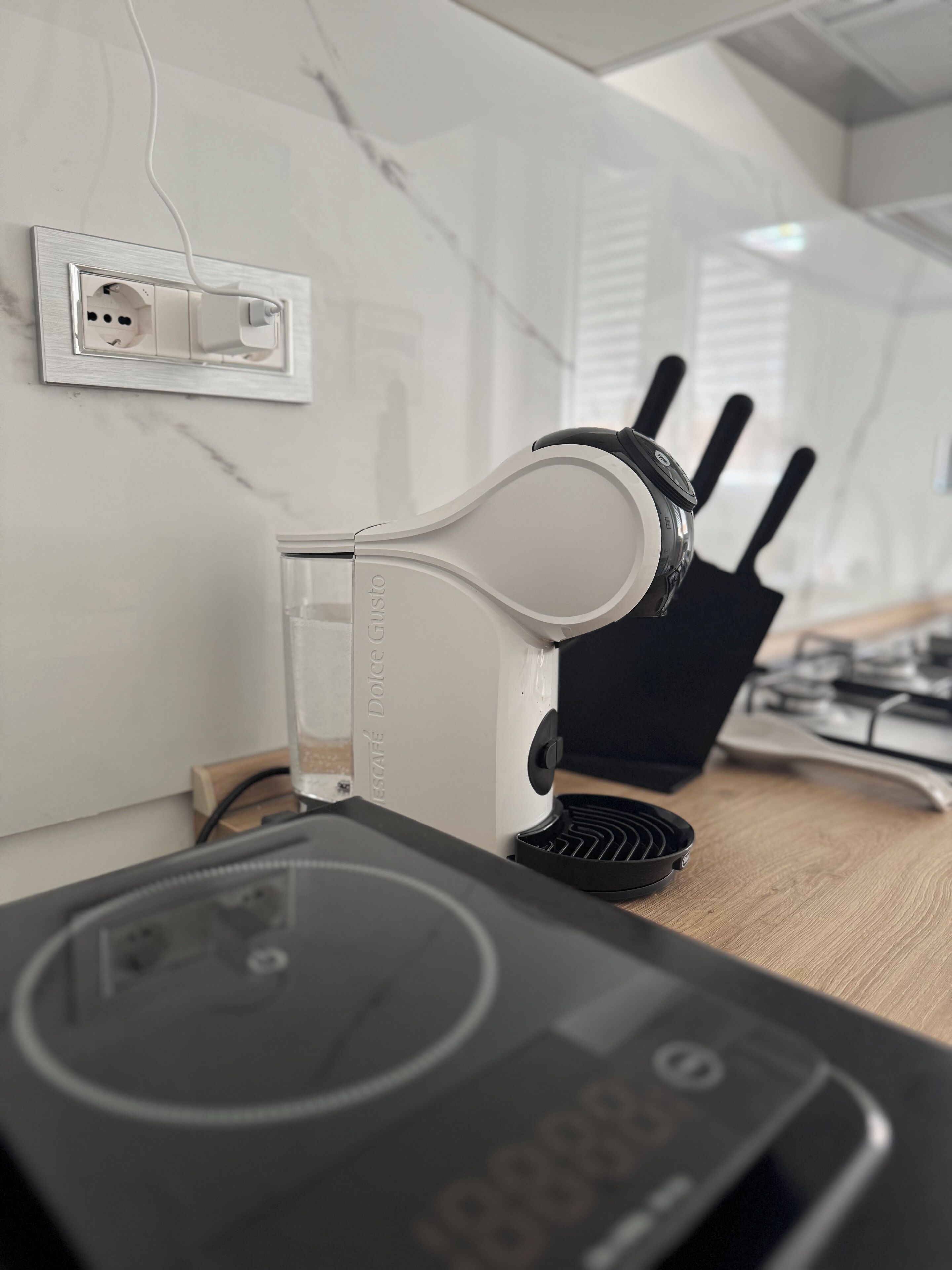 A kitchen with a modern espresso machine, a black electric kettle, and a wooden countertop.