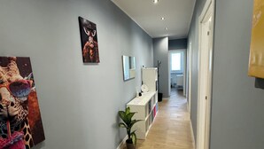 Vaalea harmaa käytävä, jossa on puulattia ja valkoinen kaappi, jossa on peili ja kello.