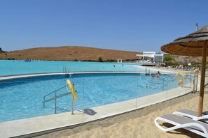 Une piscine équipée d’un poste de surveillance pour les sauveteurs, de chaises longues et d’un espace aménagé comme une plage.