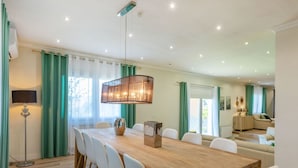 Ein Essbereich mit Holztisch, weißen Stühlen, einer Hängelampe und Blick auf ein Wohnzimmer mit Sofa und Couchtisch.
