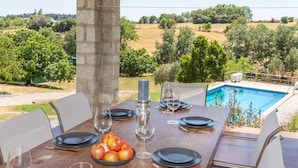 Ein Essbereich im Freien mit Tisch für vier Personen, ein Pool im Hintergrund und Blick auf die Landschaft.