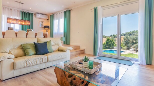 Ein modernes Wohnzimmer mit einer Couch, einem Glastisch und Blick auf einen Swimmingpool.
