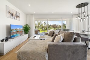 Una sala de estar moderna con un televisor de pantalla plana, un juego de sofá, una mesa de comedor y vistas a una piscina y vegetación al exterior.