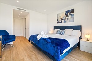 A modern hotel room with a bed, a blue chair, a bedside table, and a painting on the wall. - 3-Bedroom Lagoon Stay in Casares (Casares)