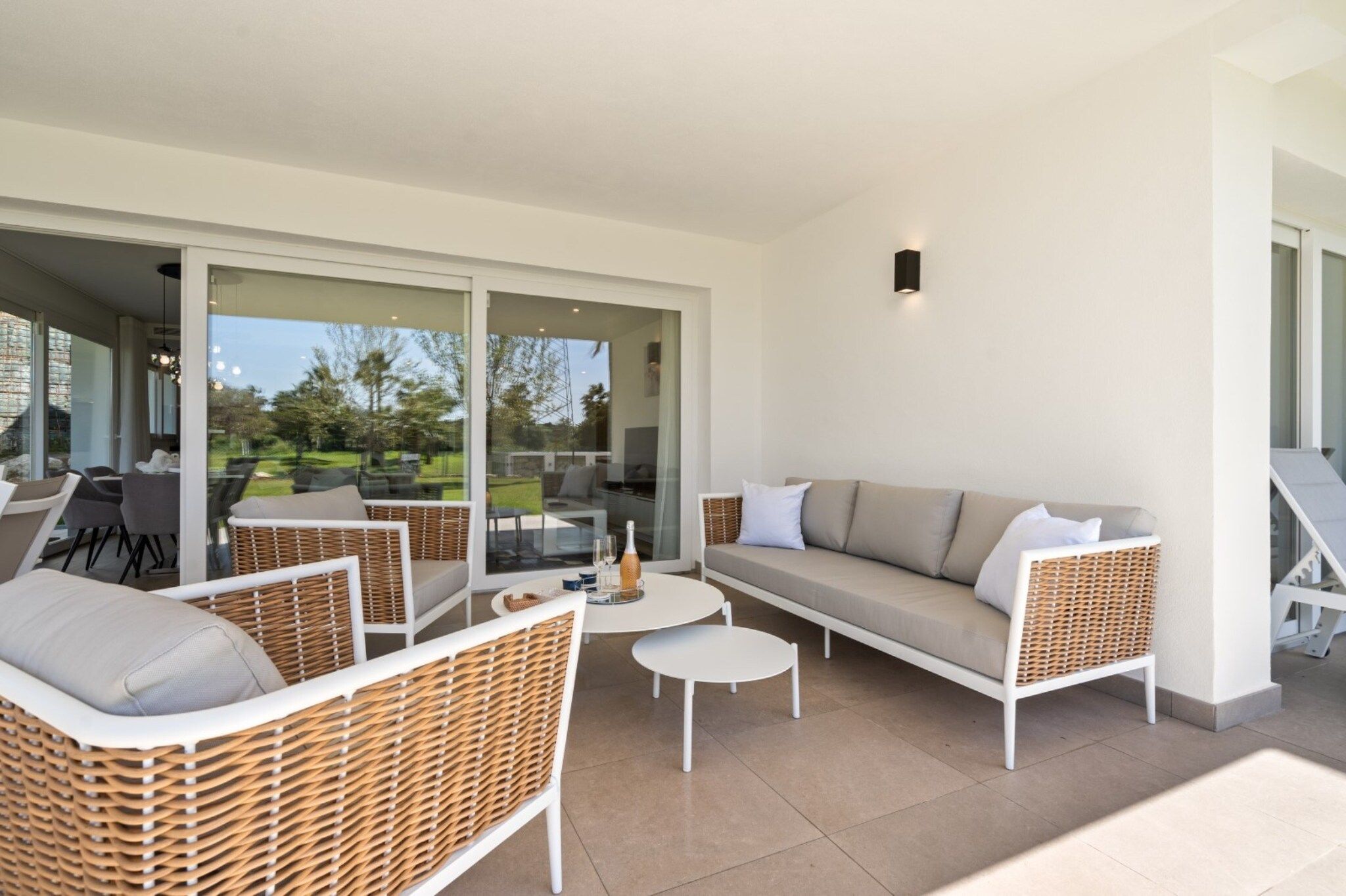 An outdoor living area with wicker furniture, a sofa, and a glass door leading to a garden.