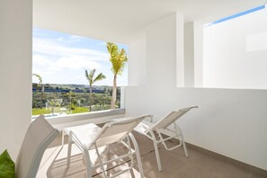 Ein Balkon mit Tisch und Stühlen, der auf eine Landschaft mit Bäumen und eine ferne Aussicht blickt.