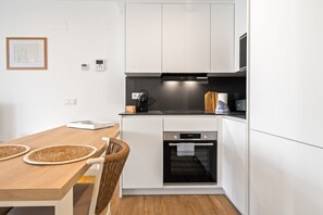 Eine moderne Küche mit weißen Schränken, einem eingebauten Backofen, einer Kaffeemaschine und einem Essbereich mit Holztisch und gewebten Unterlagen.